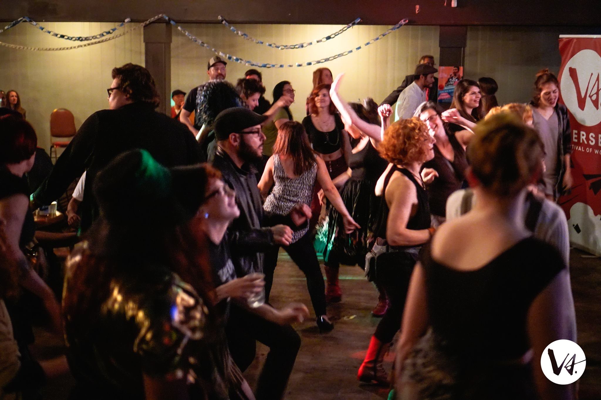 [ID: Many people dancing and moving around a room. They are smiling. /endID]