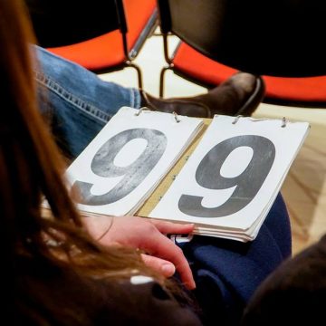 [ID: A scoreboard reading 9.9 sits on the lap of a judge/ end ID]